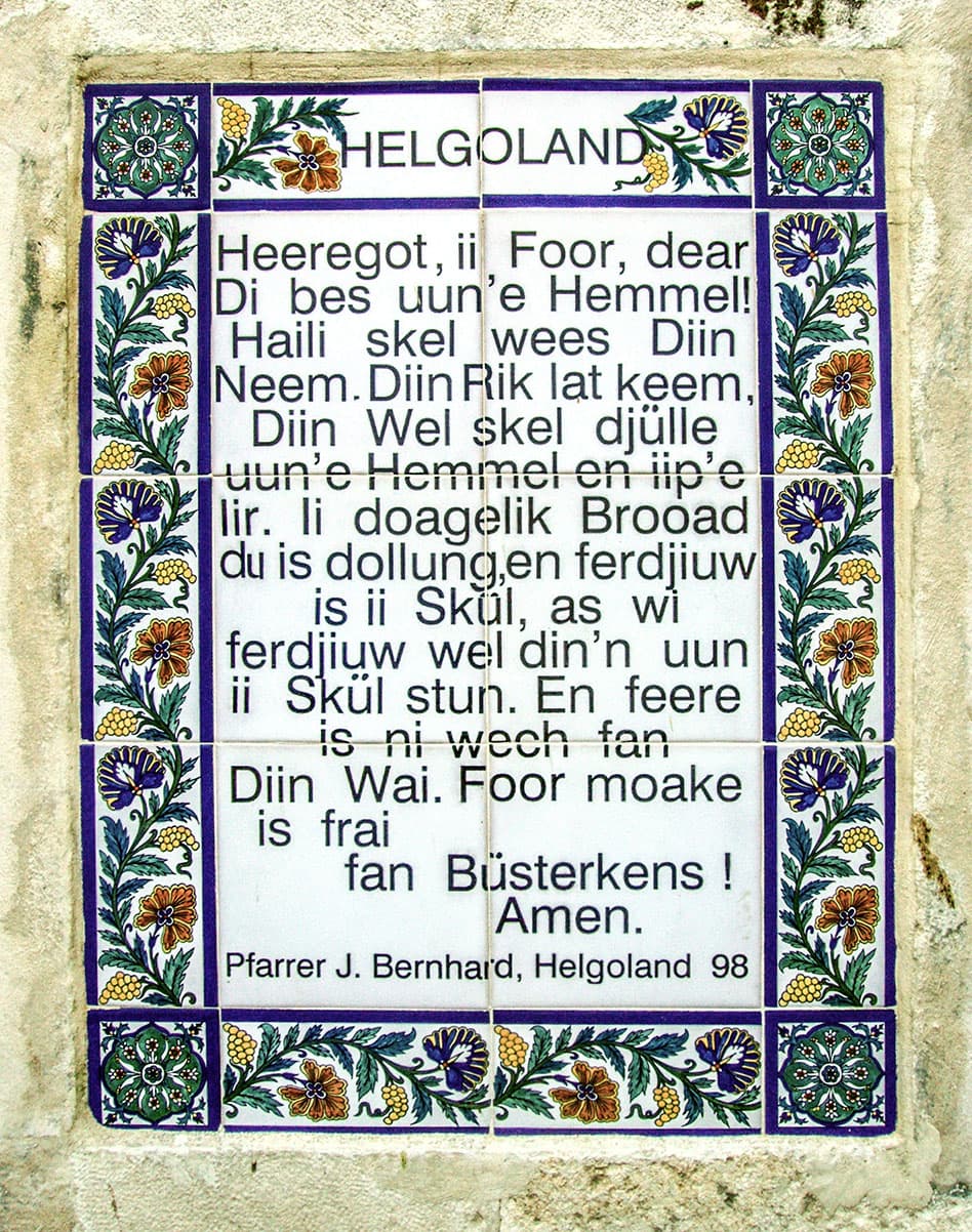 Majolikaplatte mit dem Vaterunser auf Halunder in der Paternoster-Kirche auf dem Ölberg in Jerusalem. Über dem Text steht 'HELGOLAND', unten die Signatur 'Pfarrer J. Bernhard, Helgoland 98'.