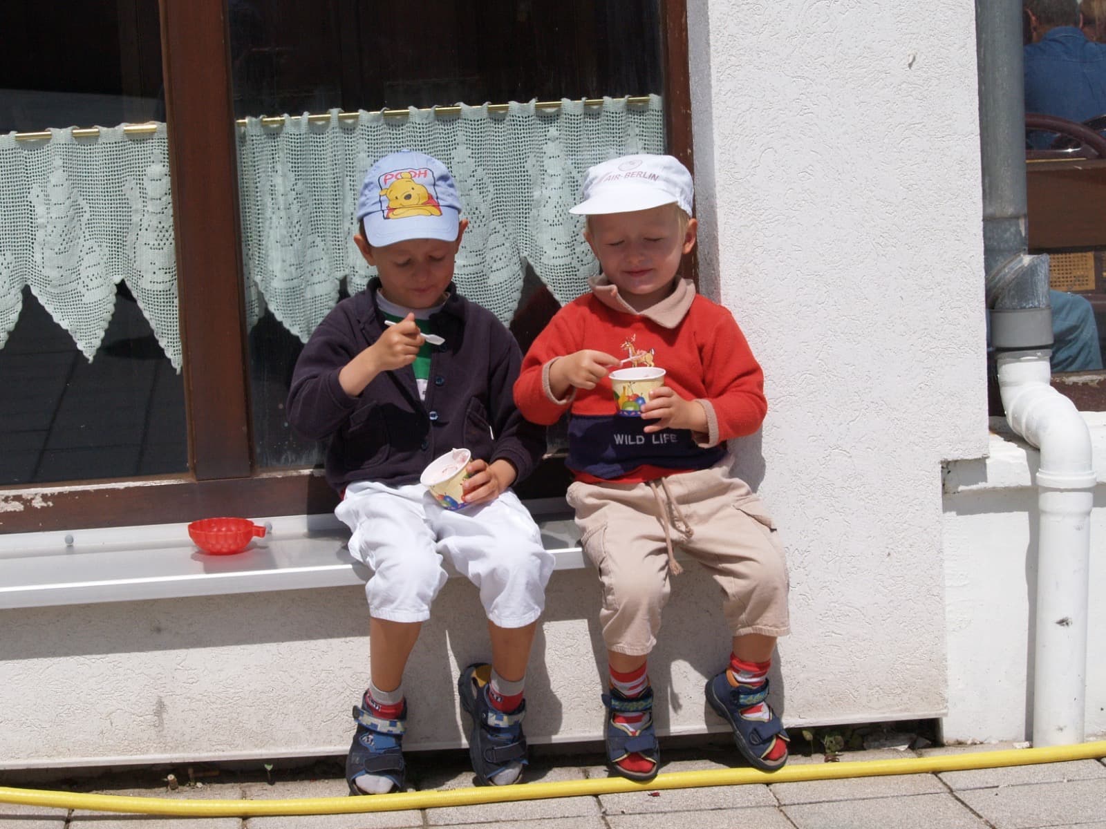 Jakob als Kind mit seinem Bruder beim Eis essen auf einer Helgoländer Fensterbank, beide mit Sommermützen.