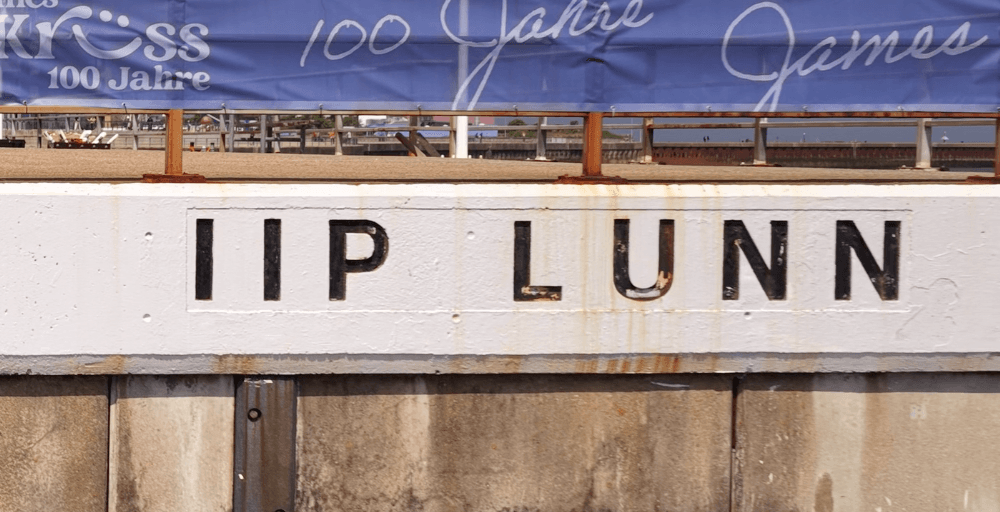 Detailaufnahme der rechten Hälfte der Helgoländer Anlegeraufschrift. Weiße Großbuchstaben 'IIP LUNN' auf grauem Beton.